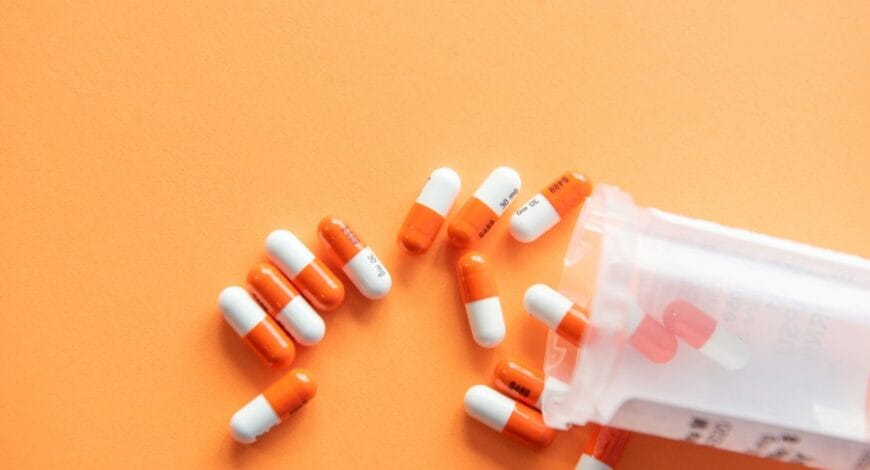 Prescription drugs on an orange background with a pill bottle.