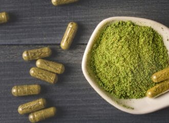 kratom powder in a bowl next to capsules