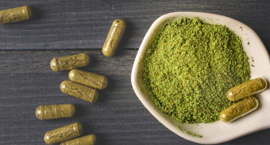 kratom powder in a bowl next to capsules