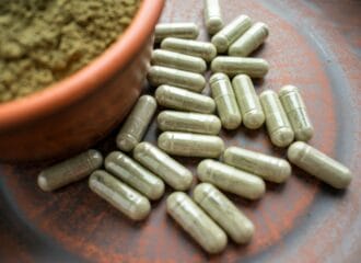 green capsules of kratom on table next to bowl of kratom