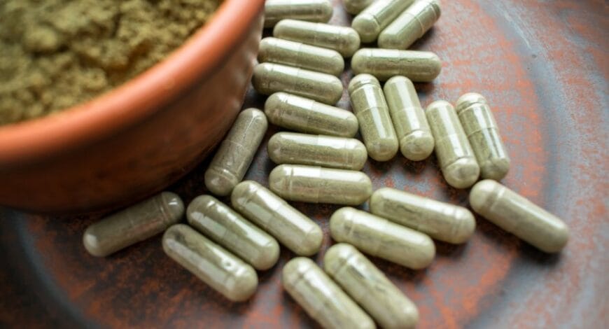 green capsules of kratom on table next to bowl of kratom