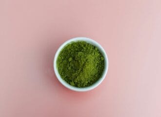 A bowl of green powder on a pink background