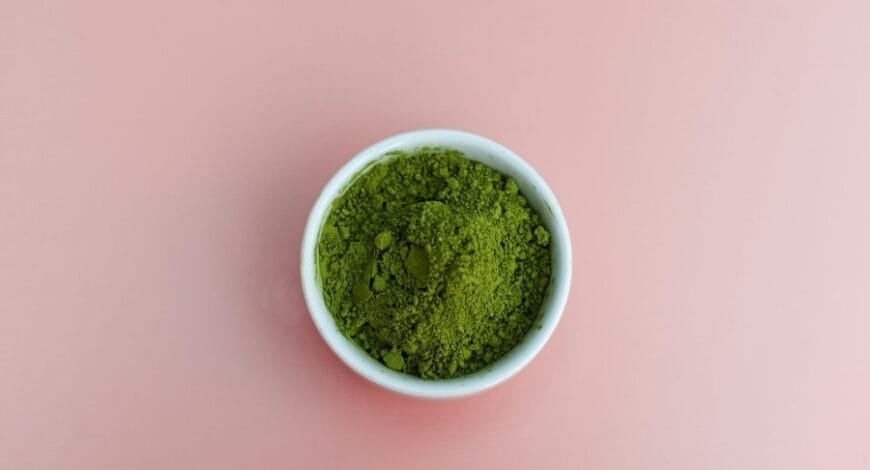 A bowl of green powder on a pink background