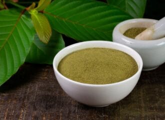 Bowl of kratom powder next to kratom leaves